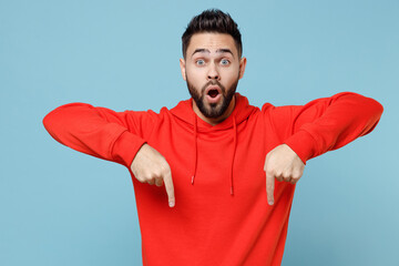 Young caucasian smiling bearded attractive man in casual red orange hoodie point index finger overhead on copy space area mock up isolated on blue background studio portrait People lifestyle concept. © ViDi Studio