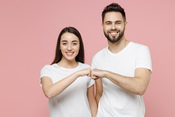 Young cheerful couple two friends man woman 20s in white basic t-shirts giving fist bump holding...