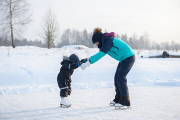 young mother teaching her little son ice skating at outdoor skating rink. Family enjoy winter on ice-rink outdoors