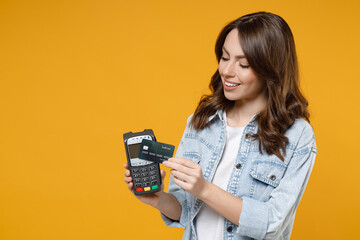 Young smiling successful woman 20s in denim shirt white t-shirt hold wireless modern bank payment...