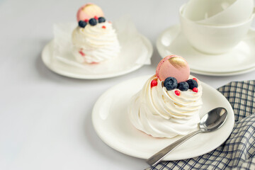 Still life Pavlova meringue cake decorated macaron on white background. Tea cups and napkin on wood table
