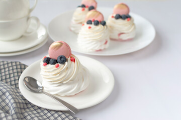 Still life Pavlova meringue cake decorated macaron on white background. Tea cups and napkin on wood table