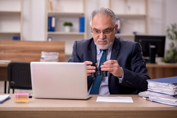 Obraz premium Old male employee auditor holding binoculars at workplace