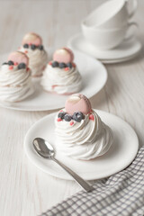 Pavlova meringue cake with fresh berries on white background. Tea cups and napkin on wood table