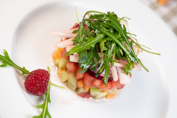 Tartare of fresh diced vegetables and salads in a white plate decorated with a raspberry , France