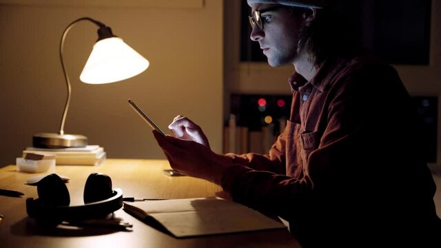 Caucasian male free lancer working from home late at night typing on cellular device writing on notepads