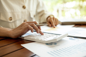 Close-up of a businesswoman using a white calculator, a financial businessman examining the numerical data on a company financial document, she uses a calculator to verify the accuracy of numbers.