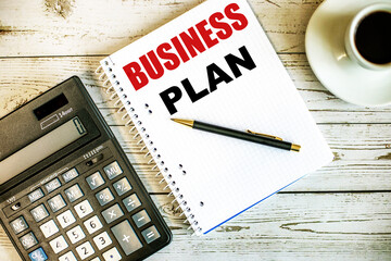BUSINESS PLAN written on white paper near coffee and calculator on a light wooden table. Business concept