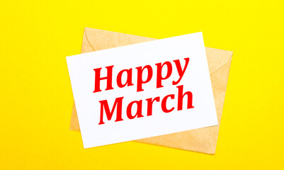 On a yellow background, an envelope and a card with the text HAPPY MARCH. View from above