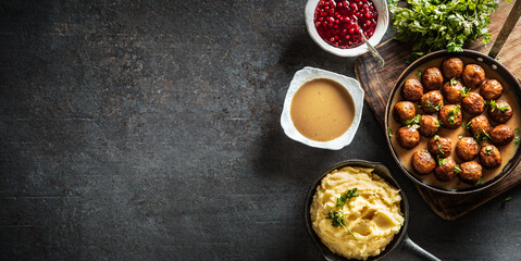 Top view of Swedish meatballs kottbullar with bowls of sauce, potato mash and cranberries on the side