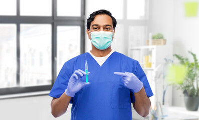 Fototapeta na wymiar healthcare, vaccination and medicine concept - indian doctor or male nurse in blue uniform, face mask for protection from virus and gloves with syringe over medical office at hospital on background
