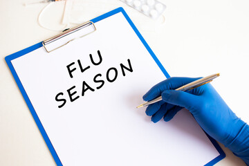Female doctor's hand in a medical glove makes an inscription FLU SEASON in a document.