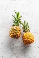 Two fresh whole pineapples with leaves on a marble surface