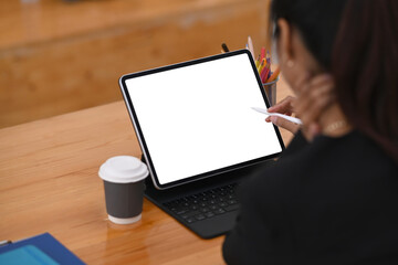 Rear view of businesswoman holding stylus pen working with computer tablet on wooden office desk.