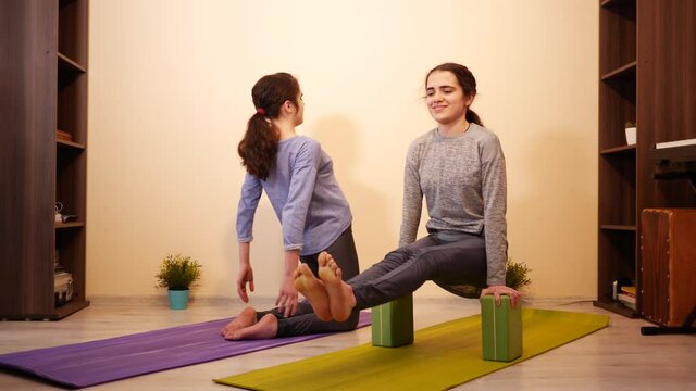 Cute teenage girls twin sisters at home doing yoga exercises workout on sport mats on a floor - body training for healthy life