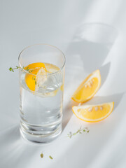 Glass of clean mineral sparkling water with ice and lemon on a white background with sunshine