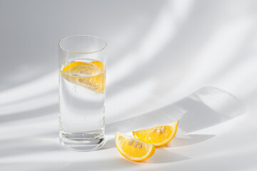 Glass of clean mineral sparkling water with ice and lemon on a white background with sunshine
