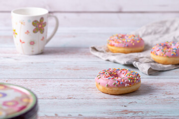 Delicious donuts with pink icing and colorful sprinkles on wooden background. Sweet pastry for a coffee klatch, as a snack for birthday party or other celebrations. Pastel colors, light and airy.