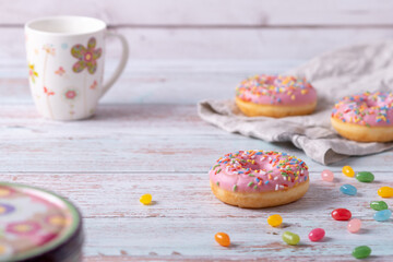 Tasty donuts with pink icing, colorful sprinkles and jelly beans on wooden background. Sweet pastry as a snack for children's birthday party or other celebrations. Pastel colors, light and airy.