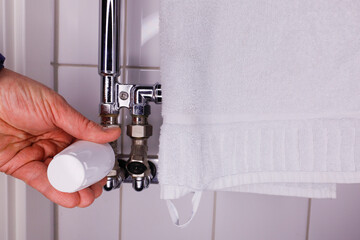 A hand checks the temperature of a hot towel rack in the bathroom.