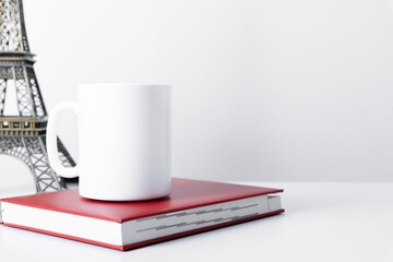 White mug mockup with workspace accessories, notebook, eiffel tower on white table. Travel and vacation concept. Front view. Place for text, copy space, mockup