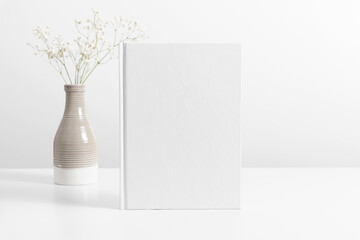 White book mockup with dried flowers in vase on white table. Front view. Place for text, copy...