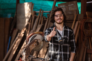 Fototapeta na wymiar portrait of happy smile young carpenter caucasian man worker thumbs up with circular saw in factor. craftsman profession in wood factory.