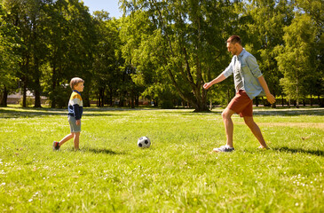 family, fatherhood and people concept - happy father and little son with ball playing soccer at summer park