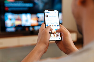 Caucasian guy using mobile phone while watching TV at home