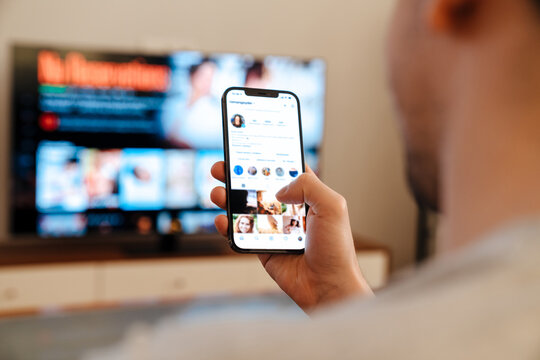 Caucasian guy using mobile phone while watching TV at home Stock Photo |  Adobe Stock