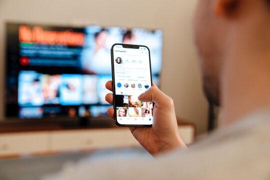 Caucasian guy using mobile phone while watching TV at home