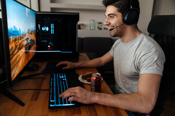 Happy brunette guy in headphones playing video game on his computer