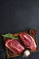 Raw organic marbled beef steaks with spices  on a wooden cutting board . Top view with copy space.