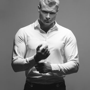 Male fashion, beauty concept. Portrait of brutal young man with short wet blond hair wearing white shirt, posing over gray background. Classic style. Studio shot