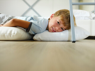 Fototapeta premium Child in pajamas sleeping in his bed without blankets, illuminated by the light that filters through the window