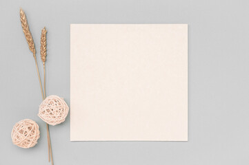 Square invitation card mockup with dried golden ears on a neutral color table. mockup White paper empty blank. minimalistic design