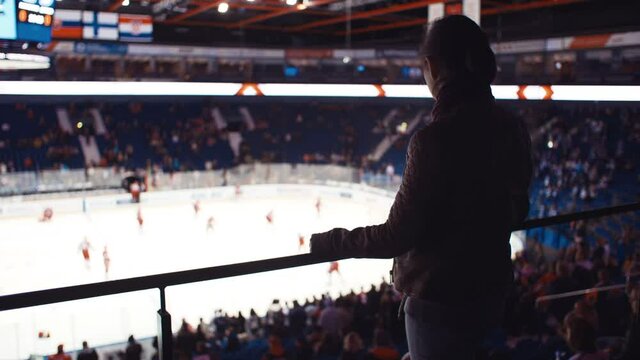 Silhouette of woman standing and watching players during practice. Moment before start of ice hockey match. Concept of sport, entertainment.