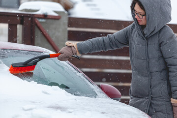 Young woman brushing snow from car after heavy snowfall