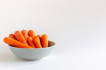 Group of carrots in a blue bowl on white background, copy space