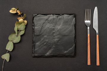 Mockup Blank board and cutlery. Knife and fork with black stone board for menu or recipe text and gold eucalyptus branch. Flat lay with mockup food menu on black table