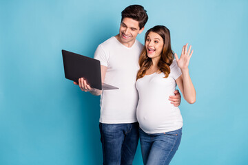 Photo of optimistic pregnant couple talk laptop wear white t-shirts isolated on cyan color background