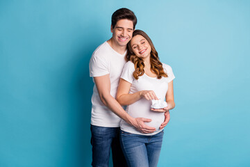 Photo of young happy smiling dreamy good mood couple pregnant wife hold little booties isolated on blue color background