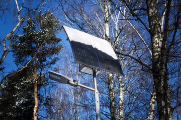 Solar powered street lamp in the park. The solar panel is half covered with snow.