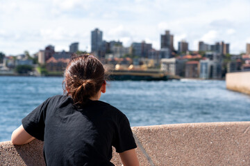 View of young girl from behind looking at a ferry in harbour sail by