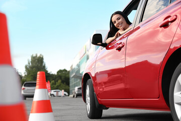 Young woman in car near traffic cones outdoors. Driving school exam