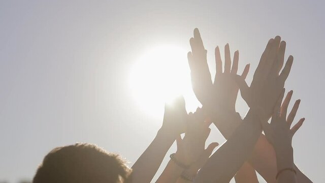 Close up, people raise their hands up to the sky and join their palms together in the bright summer sun. Strengthening team spirit by joining hands together. 
