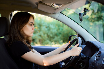 Young sad girl driving car on a summer day. Female driver with a bad mood inside the automobile.