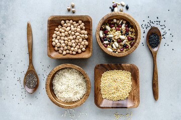 Variation von Reis und Hülsenfrüchten in Holzschüssel und Löffeln. Rustikaler grauer Tisch, Flat lay, planzliches Protein.