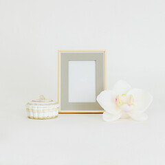 Isolated shot of empty golden frame mockup next to a jewelry box and orchid bud on white background