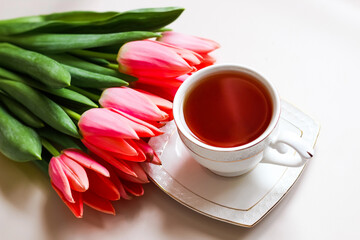 Fototapeta na wymiar Cup of tea with a bouquet of pink tulips. Minimalism of breakfast composition. Spring concept.
